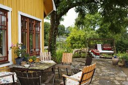 Garden furniture and a swinging chair on a natural stone patio in front of a yellow wooden wooden house