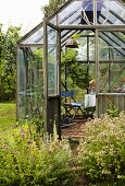 Gewächshäuschen in Holzglaskonstruktion und Garten mit blühenden Wiesenblumen