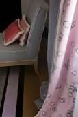 Kissen auf grauem Sessel vor rosafarbenem Vorhang