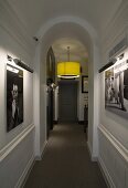 Ceiling lamp with a green shade in a hallway with a rounded arch and photos on a wood paneled wall