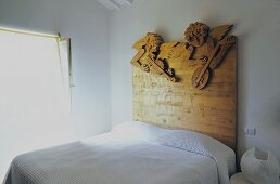 White bedroom with a double bed with a wooden headboard with carved angels