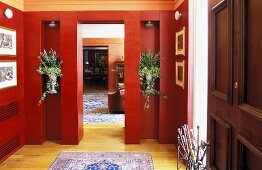 Elegant lobby with red paneled walls and flowers in niches with a view into a living room