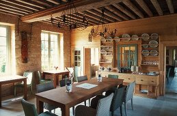 Spacious dining room with a wooden beam ceiling in a country home, long dining table with wicker chairs