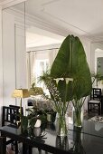 Palmenblatt und tropische Blume in Vase auf einem schwarz glänzendem Wandtisch vor der Spiegelwand