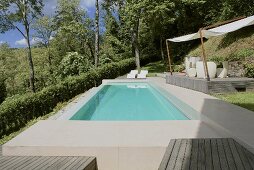 Turquoise water in a pool edged with stone in a garden and a covered wooden deck with patio furniture
