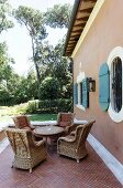 Wicker chairs on a terrace with a herringbone pattern in front of the facade of a Mediterranean villa