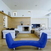 Blauer Diwan und weiße Sofagarnitur im offenen Wohnraum mit holzvertäfelter Wand und Kamin