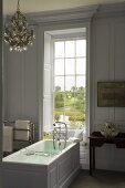 An elegant bathroom in a country house with a free-standing bathtub in front of a window with a view