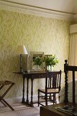 A bedroom with a table lamp on an antique wall table standing against a wall hung with floral wallpaper
