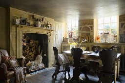 A country house kitchen in the basement with old wooden chairs and a table in front of a large fireplace stacked with wood