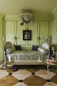 Elegantes antikes Bett vor grüner Holzvertäfelung und bemalter Holzboden