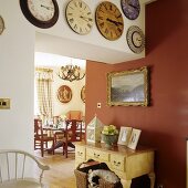 A collection of antique wall clocks above a doorway with a red wall and view onto a dining table