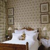 An antique wooden bed in a traditional English bedroom with wallpaper and matching curtains