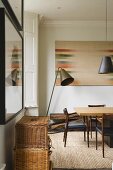 A stack of baskets in front of a brass floor lamp and a dining area in the corner of the room