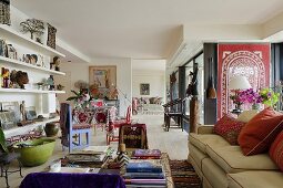 An open-plan living room with colourful furniture and a light-coloured upholstered sofa with red cushions