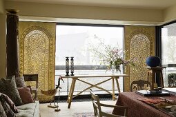 Ethnoflair im Wohnraum - heller Holztisch und folkloristische Tücher vor Fensterfront