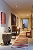 A long hallway with ceiling spotlights with chairs along the wall and a stripy rug