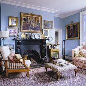 A blue-painted fireplace room with an upholstered occasional table and armchairs on an oriental rug