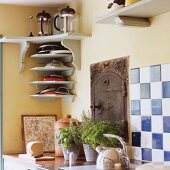 A corner of a kitchen with a light grey shelf and pots of herbs on the work surface