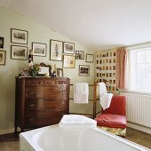 An attic bathroom with an antique wooden chest of drawers and towels next to a red chair