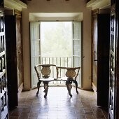 An antique wooden bench in front of open window shutters in the hallway of an old Spanish country house