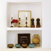 A concrete whitewashed wall niche with candle holders, busts and jars