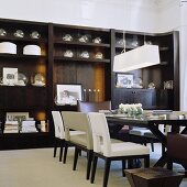 An art deco style dining room with a pendant lamp with white shade in front of a dark wooden cupboard displaying a collection of glass balls