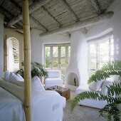 Wohnraum im tropischen Ferienhaus mit Kamin und weisser Sofagarnitur unter rustikaler Holzdecke