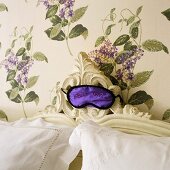 Sleeping mask on a headboard in front of wallpaper with a floral pattern on the wall