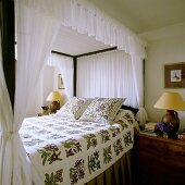 A four poster bed with a white canopy, a floral throw and matching cushions