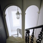 A steep flight of stairs with archways at the bottom with a view of a ceiling lantern