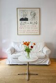 Flowers on a bistro table with metal base in front of a white sofa and a drawing on the wall