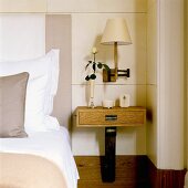 A bedside table with a drawer and a dark wooden foot in front of a white wood panelled wall