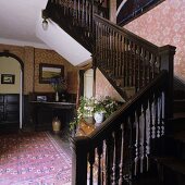 Hallway of a country house with a flight of dark wooden stairs and red-patterned wallpaper