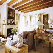 Small items of antique furniture set around a sofa in a comfortable fireplace room with a wood beam ceiling
