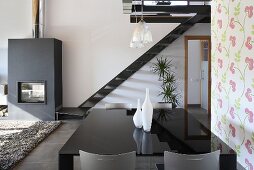 An open living-room-cum-dining-room with a black shiny table in front of a flight of stairs and a fireplace