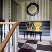 Künstlerisch bemalte Stühle vor Streifenwand im Treppenhaus