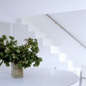 A white room with a vase on a table and a flight of stairs with a stainless steel banister rail