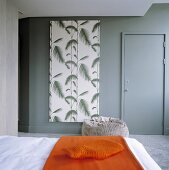 Orangefarbene Tagesdecke auf Bett und grau getönte Wand mit Tür