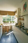 Schmale Küche - Küchenzeile mit weissen Schränken und Essplatz mit Kräutertöpfen auf Fenster