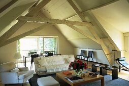 A converted attic room with wood beams and a coffee table and a sofa in front of a window
