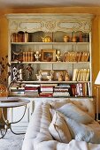 An antique dresser of books against a coloured wall and a light-coloured upholstered sofa