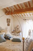 A white metal four poster bed with a bedside table in an attic bedroom with a wood beam ceiling