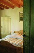 A view into a bedroom in a country house with a wooden bed and a rustic wood beam ceiling