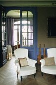Wohnraum im Jugendstil - weiße Polstersessel vor blauer raumhoher Glastür mit Blick in Nebenraum