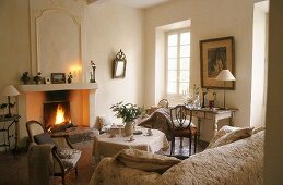 A light coloured living room in a country house with antique chairs and a table in front of a fireplace
