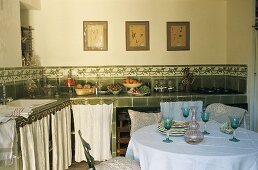 Landhausküche - Weingläser auf Tisch vor Küchenzeile mit grünen Fliesen und geschlossenen Vorhängen vor Unterschränken