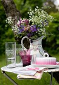 Glasses and butter dish in front of a pitcher filled with garden flowers