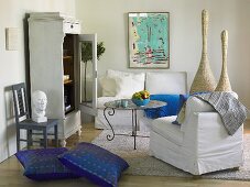 weiße Sofagarnitur mit blauen Bodenkissen und Vitrine mit offener Tür im Landhausstil