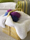 Basket with sheepskin throw blanket, balls of wool and knitting needles
